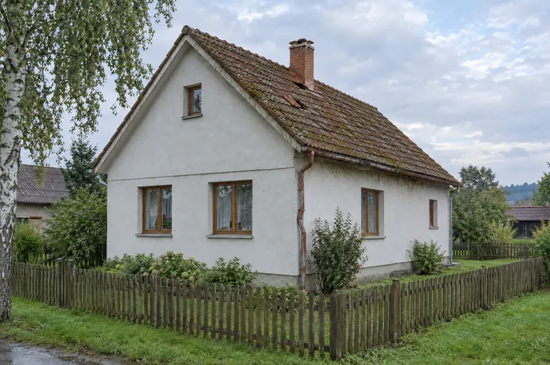 Rodinný dům před opravou: stará vybledlá taška s mechem, u komína ujetá a chybějící taška, rezavý prověšený žlab.